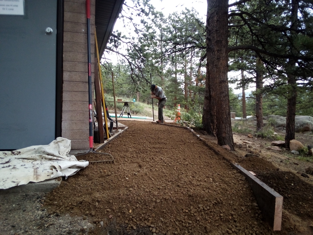 A man is working on a dirt path in front of a house.