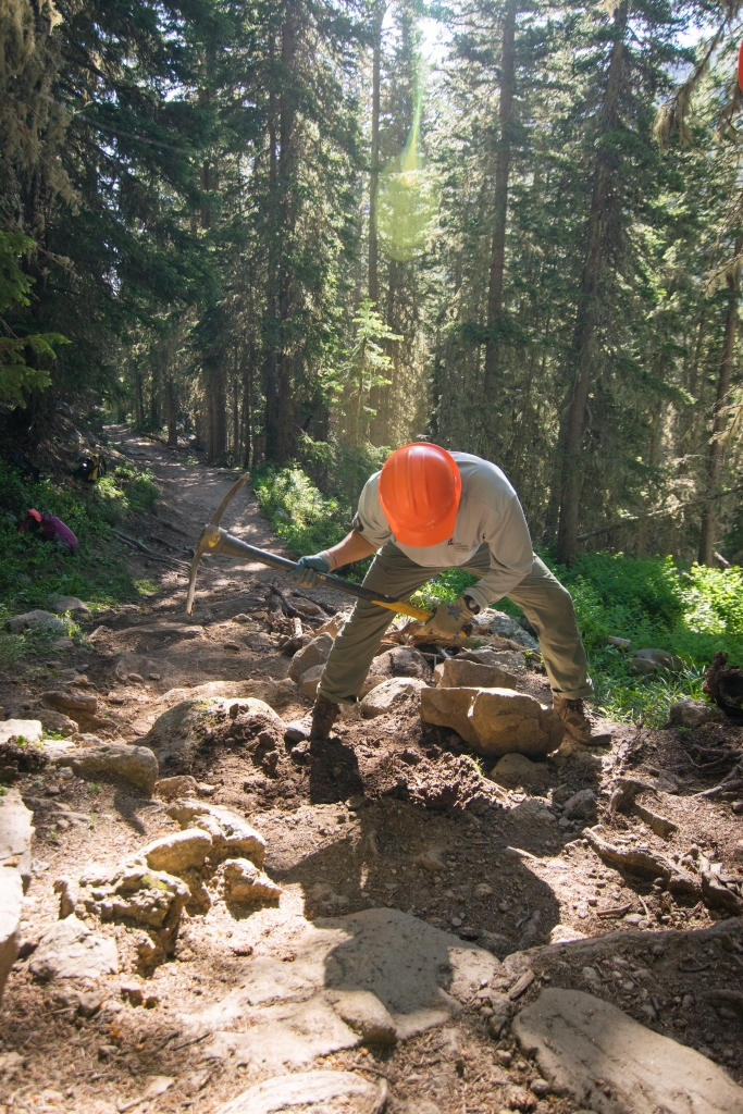 A man in an orange hat is bending down on a rocky trail.