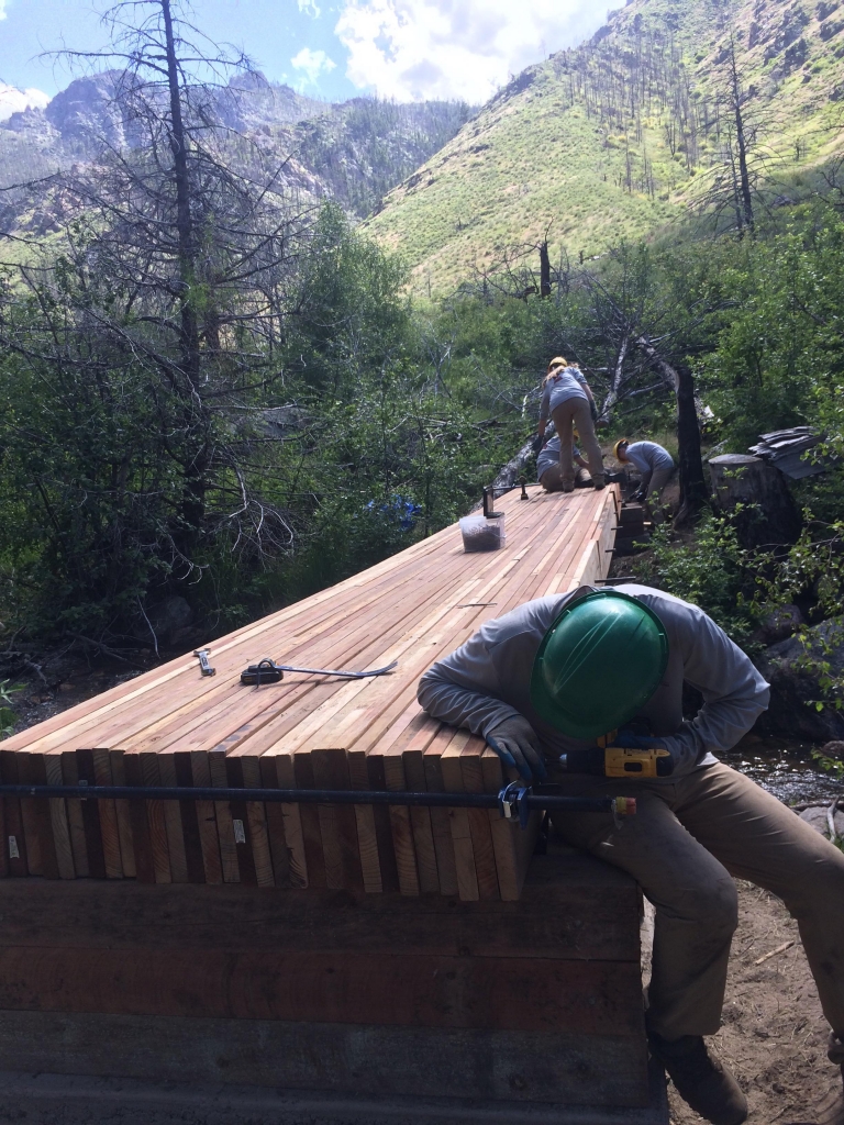A group of men working on a wooden bridge in the mountains.
