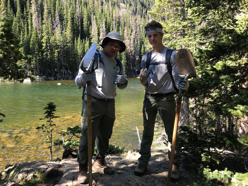 Two men standing next to a lake with shovels.