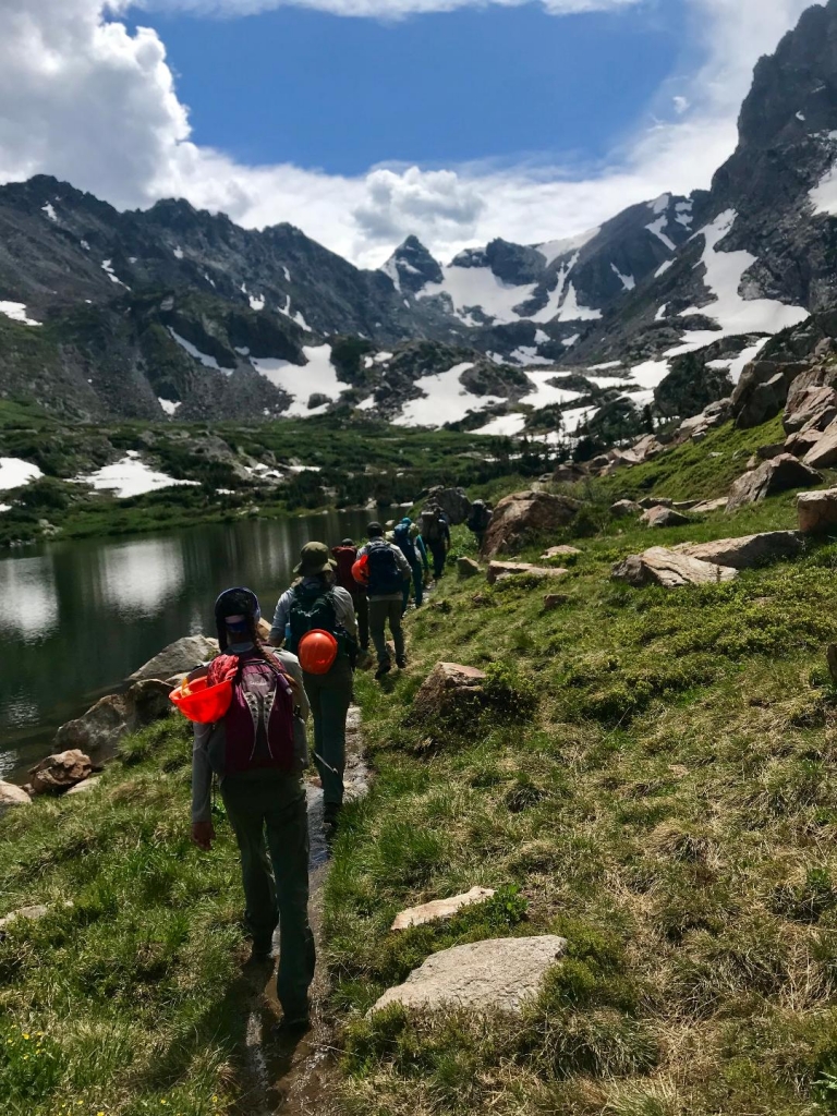 A group of hikers hiking along a trail near a lake.