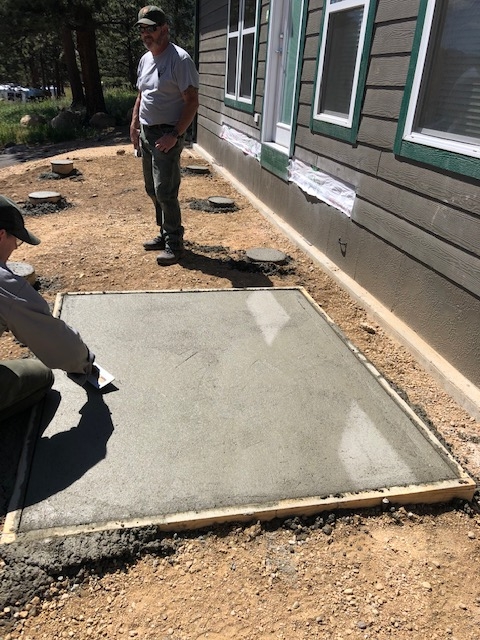 Two men working on a concrete patio in front of a house.