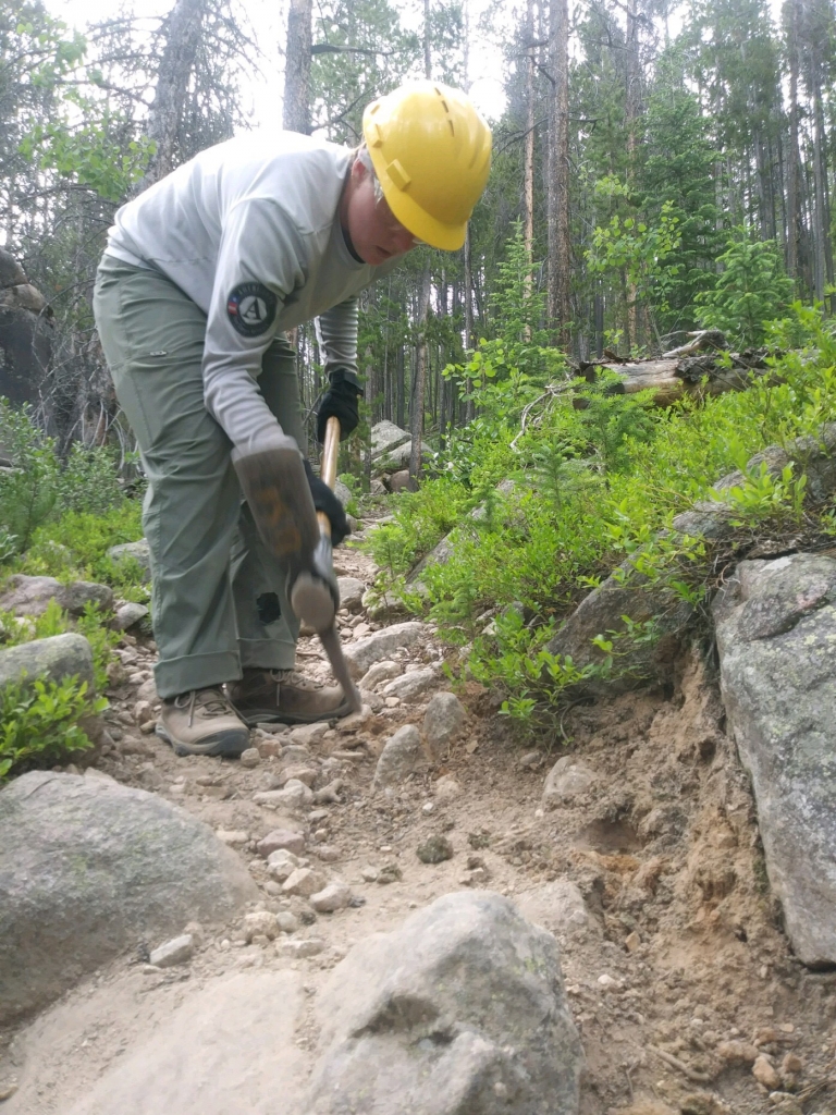 A man in a hard hat working on a trail with a shovel.