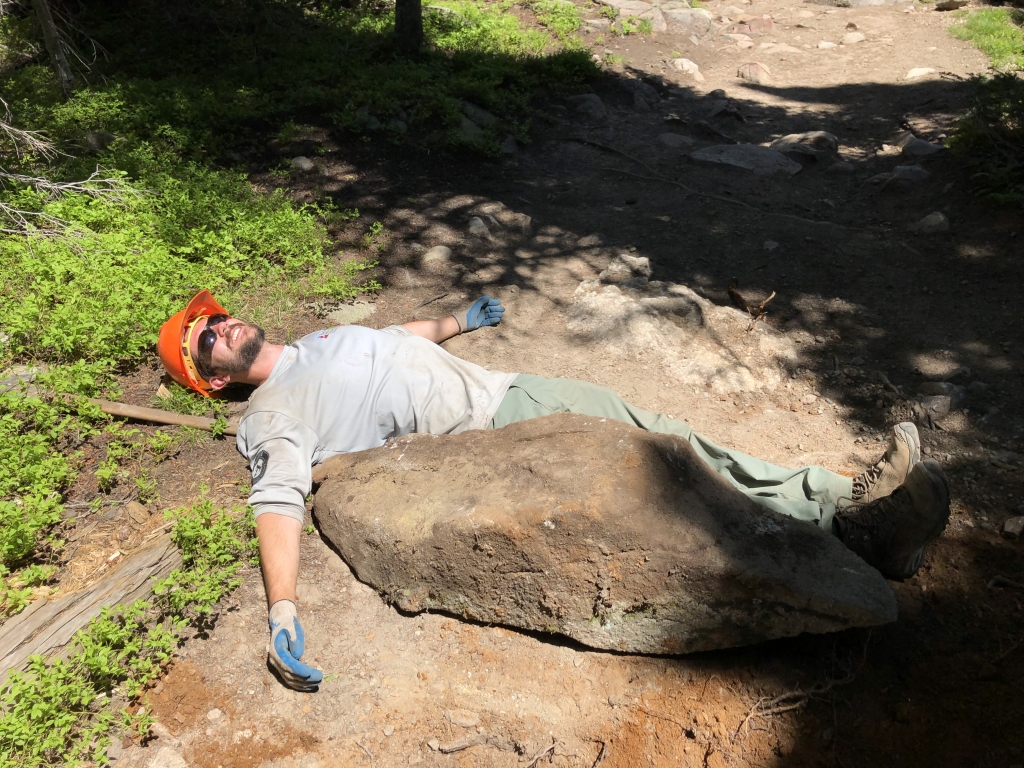 A man laying on a rock in the woods.