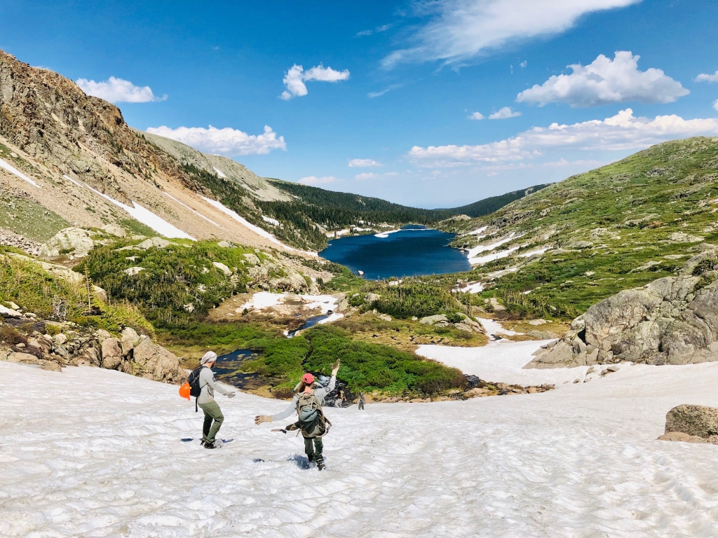 Two people hiking up a snowy mountain with a lake in the background.