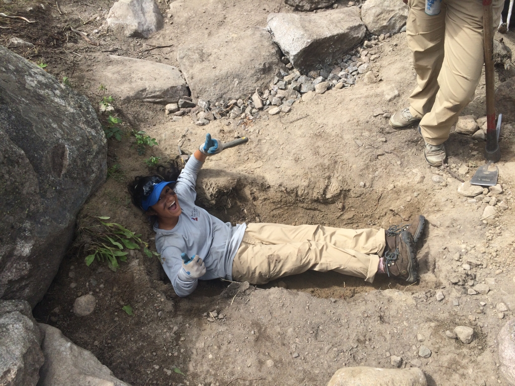 A man laying in a hole with a shovel.