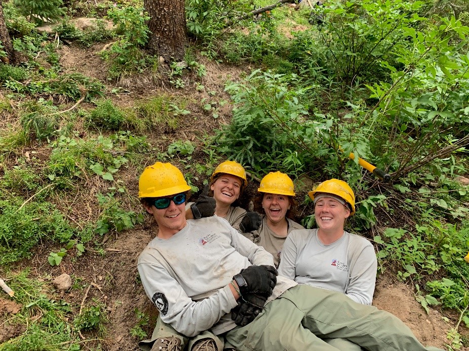 Four people in hard hats laying down in the woods.