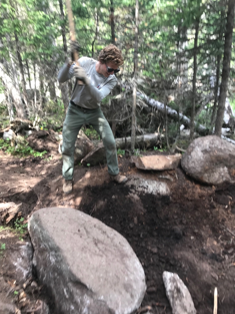 A man is hitting a rock in the woods.