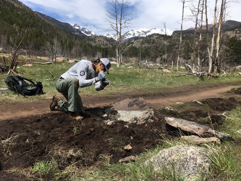 A person in a uniform and cap examining the ground