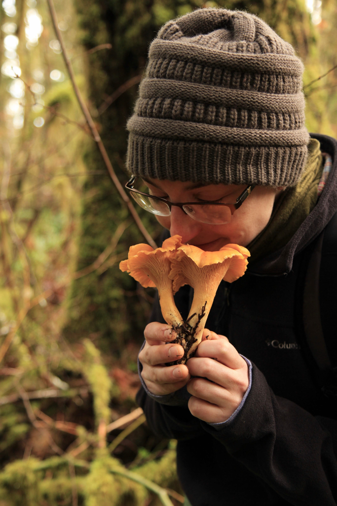 A woman is smelling a mushroom in the woods.