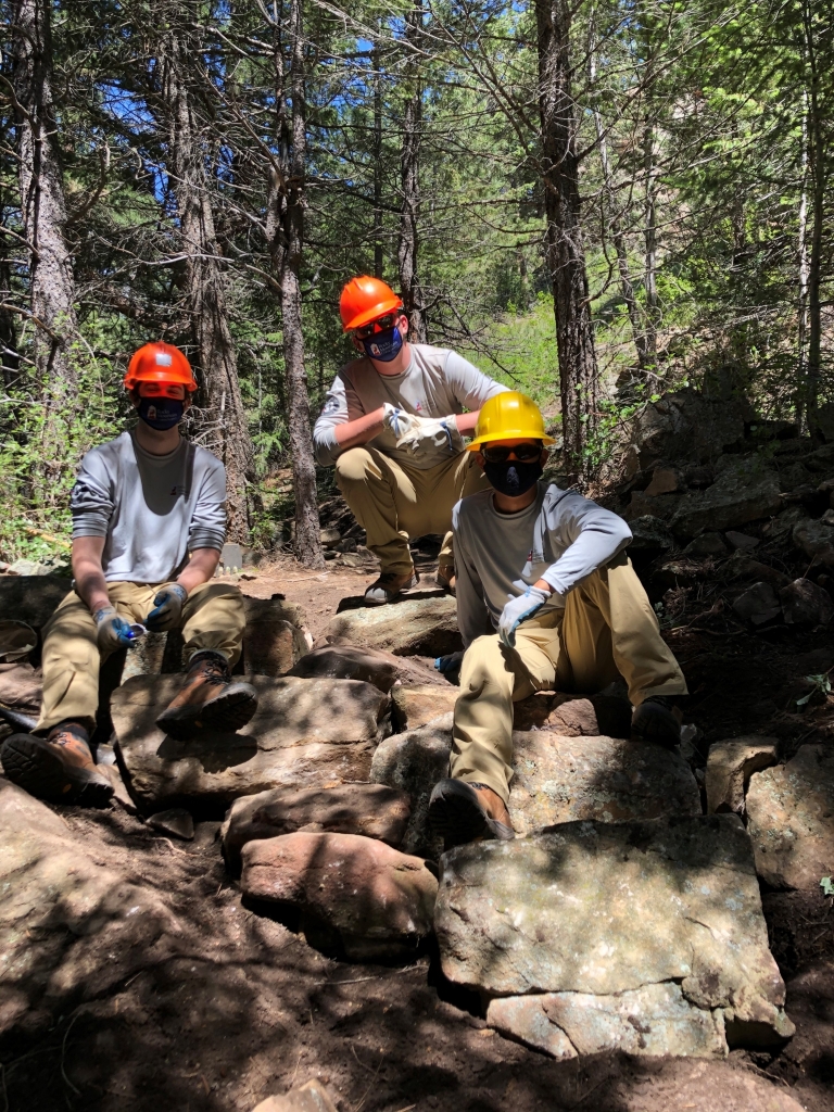 Three men posing on rocks in a wooded area.