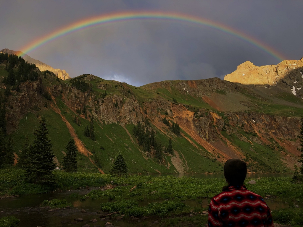 A person observing a vibrant rainbow arching over a mountainous landscape