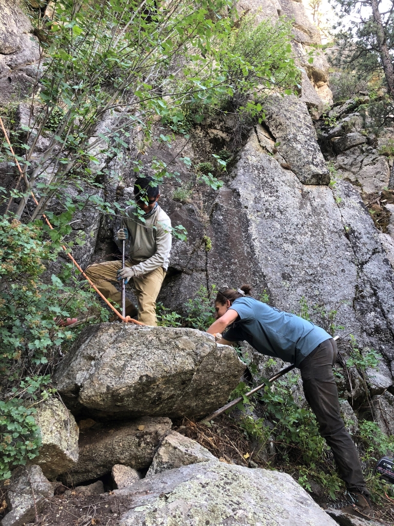 Two people working on a rock in the woods.