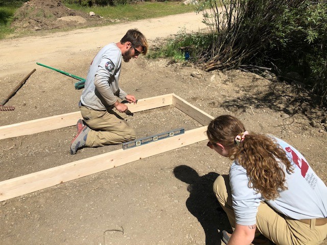 Two people working on a wooden frame in the dirt.