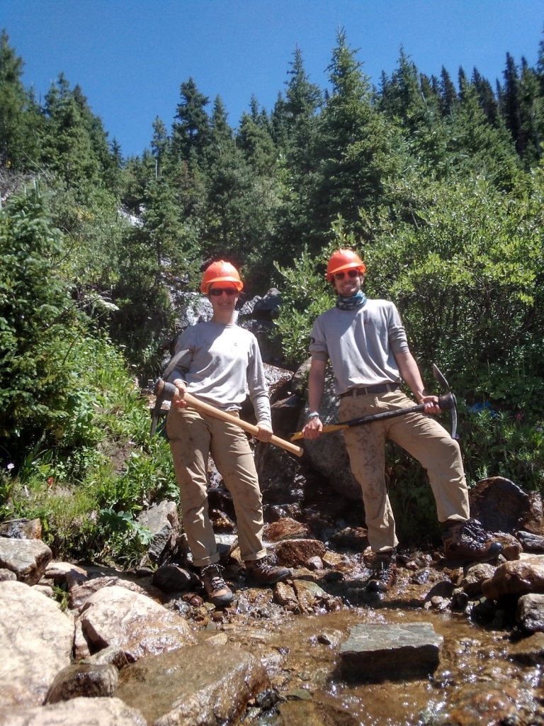 Two men in hard hats standing next to a stream.