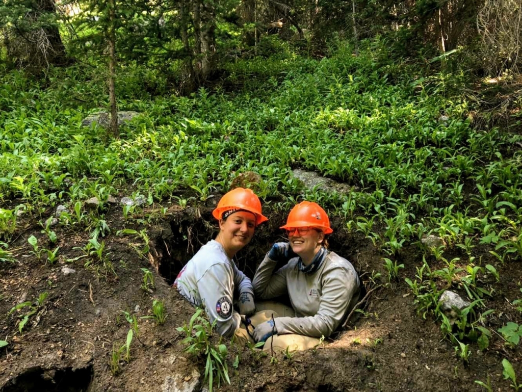 Two people sitting in a hole in the woods.