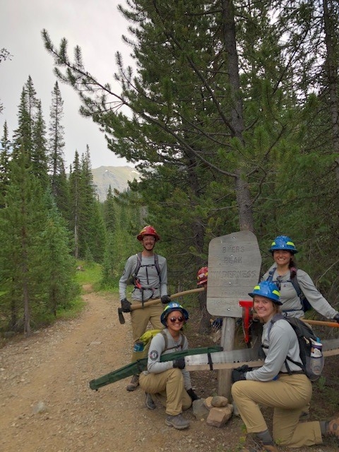 A group of people posing with a sign on a trail.
