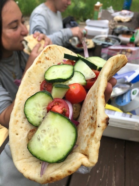 A woman is holding a pita with tomatoes and cucumbers.