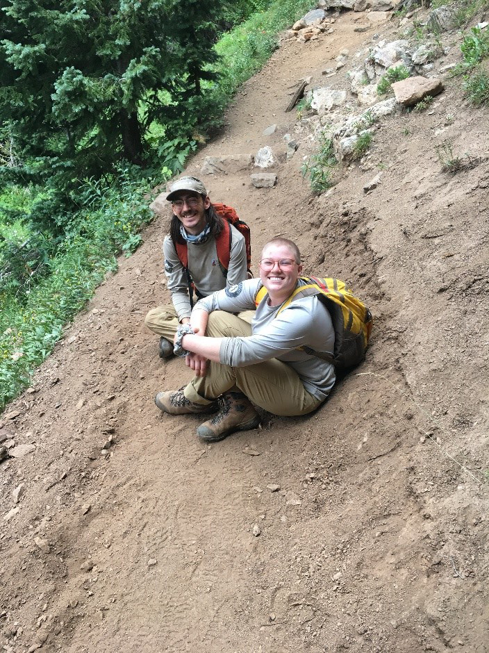 Two people sitting on the side of a trail with backpacks.