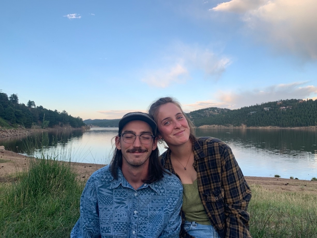 A young couple smiling at the camera, sitting by a lakeside