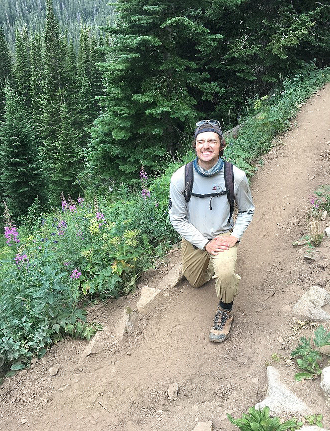 A man crouching on a trail in the mountains.