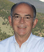 A man in glasses is smiling in front of a mountain.