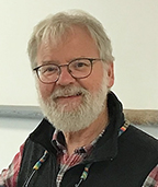 A man with glasses and a beard in a classroom.