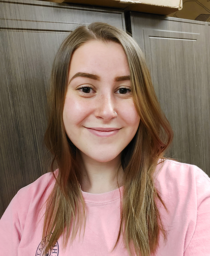 A young woman smiling in a pink shirt.