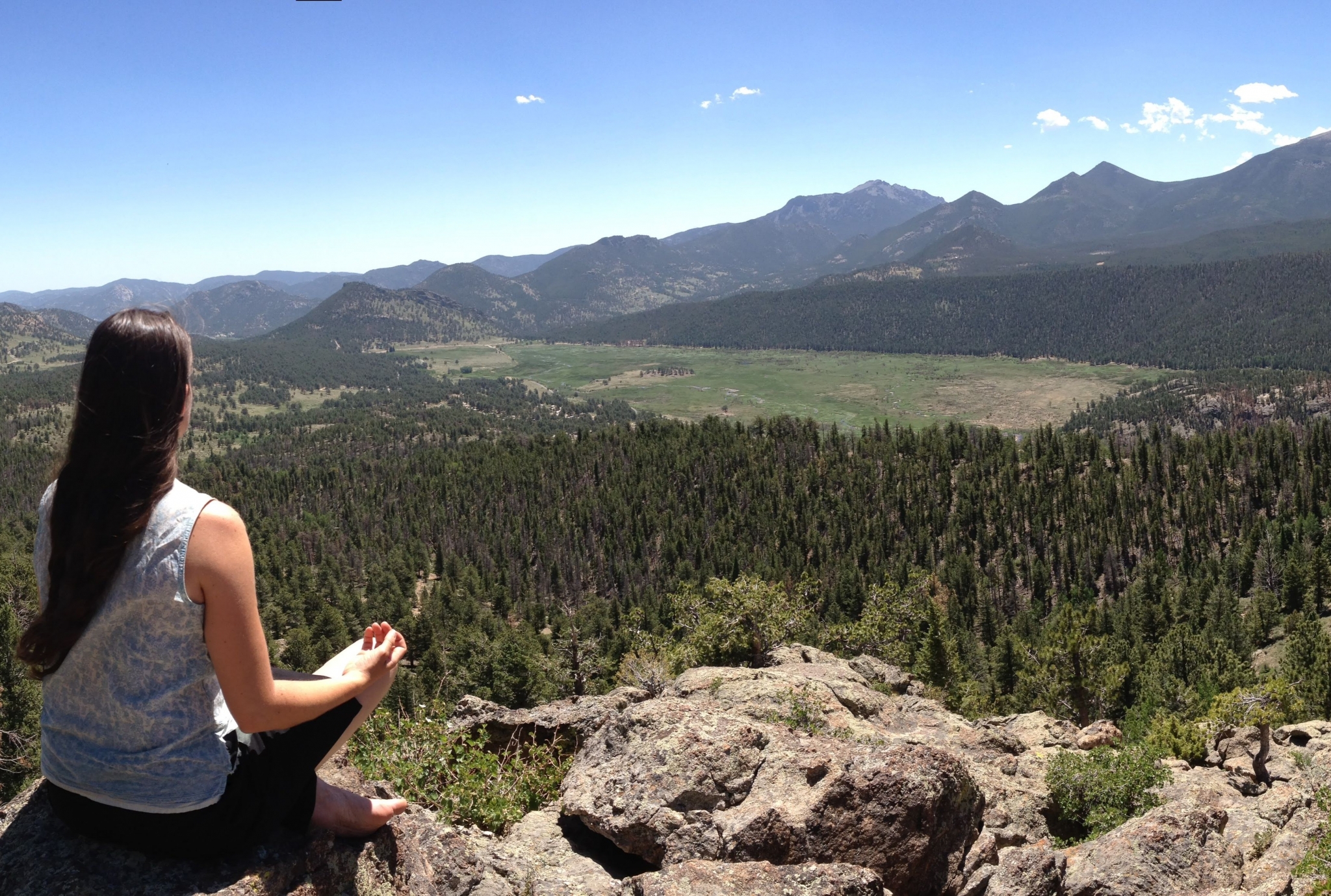 A woman sits on top of a mountain and meditates.