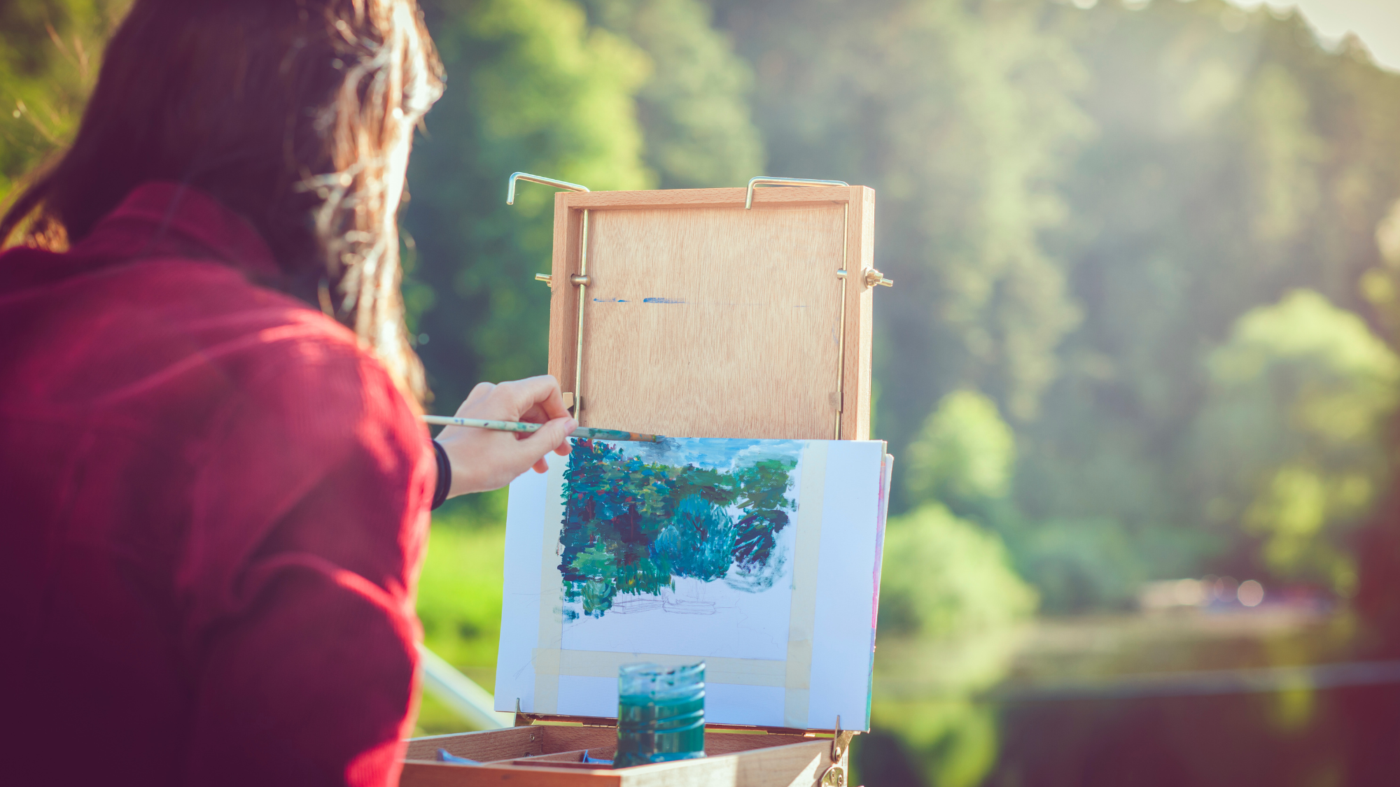 A woman is painting on an easel in front of a river.