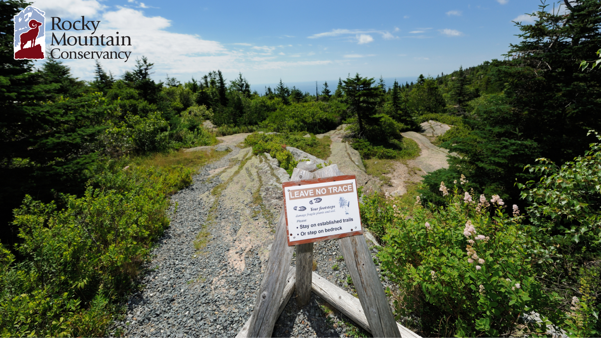 A sign on a trail with a view of the mountains.