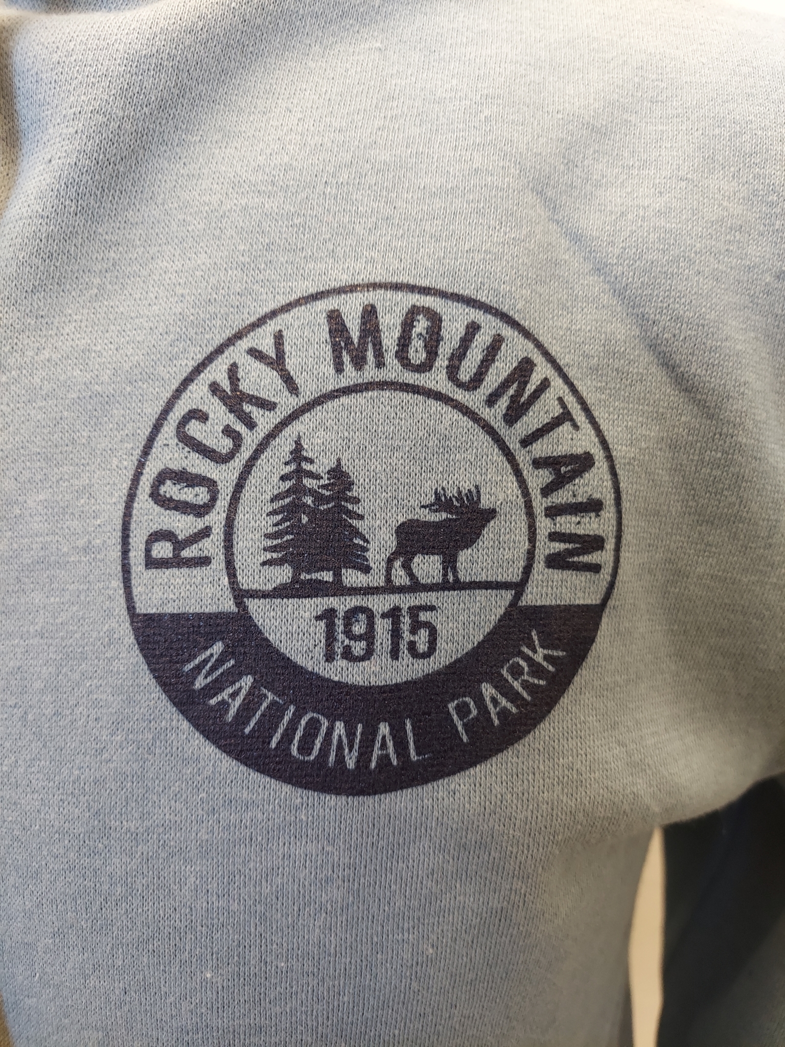 Rocky Mountain National Park logo on a RMNP Zip-Up Blue sweatshirt.
