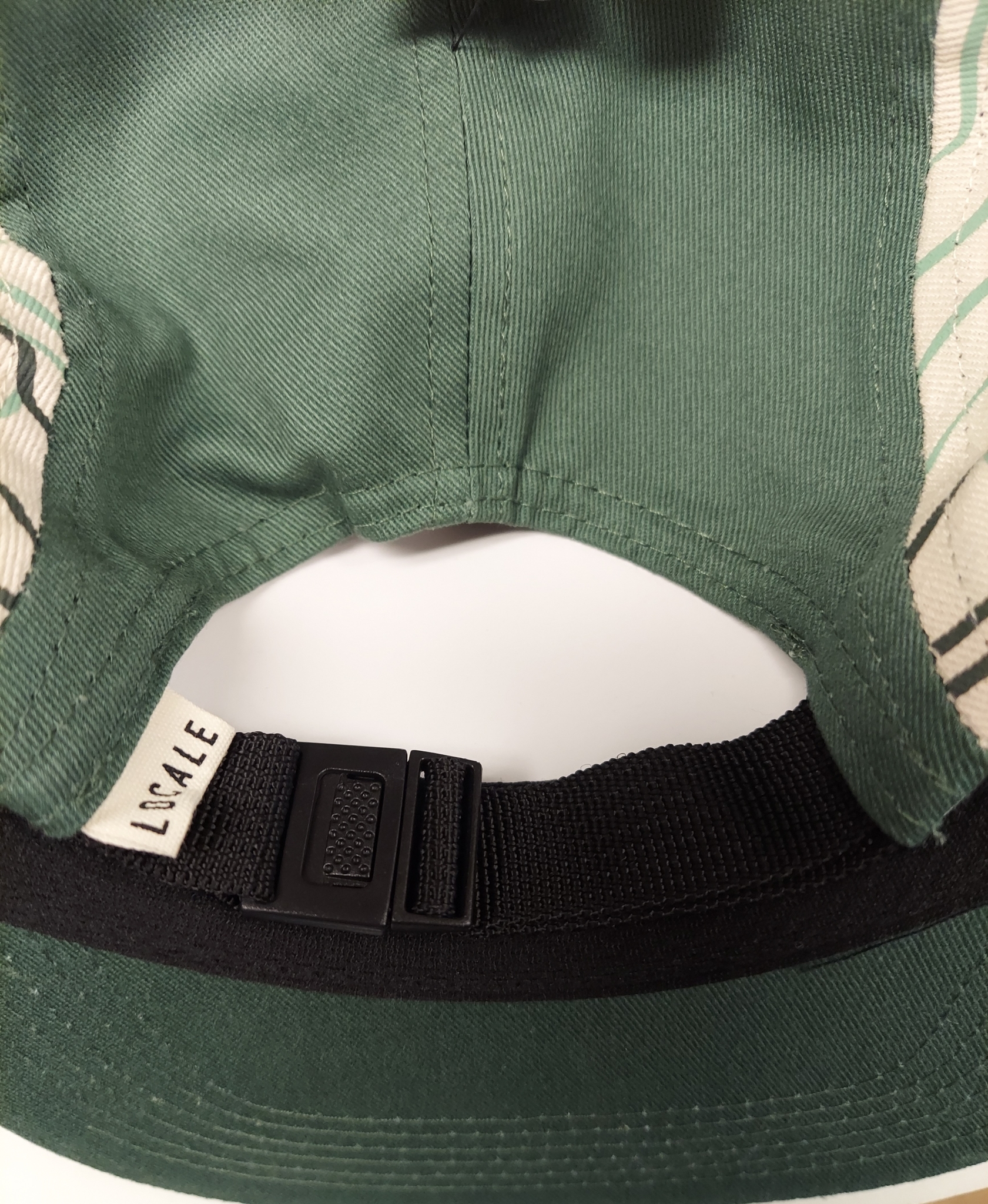 Close-up of the inside of a Hat - RMNP Green Camper showing the black adjustable strap and the tag with "LOCALE" written on it.