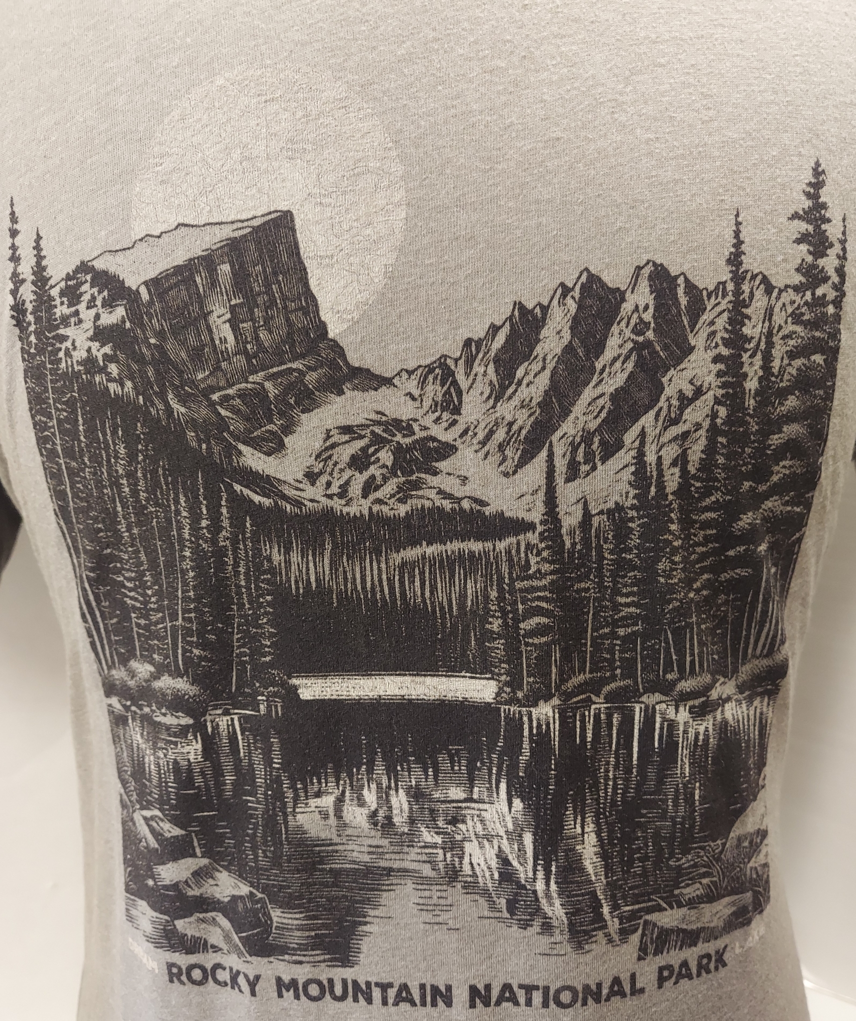 Gray T-shirt featuring a black and white illustration of Rocky Mountain National Park's Dream Lake, showcasing pine trees, mountains, and a moon in the background.