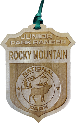 An ornament, named the "RMNP Junior Ranger Badge," features a wooden design with the words "Junior Park Ranger Rocky Mountain National Park" and an engraved image of a deer and trees.