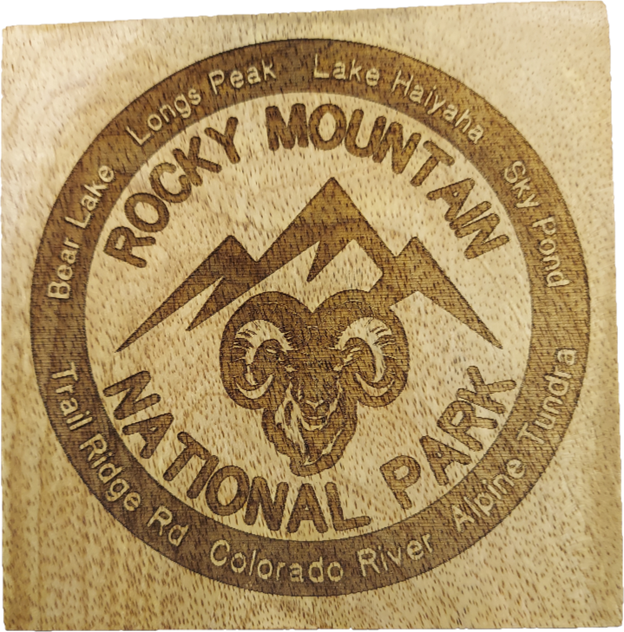 A coaster from the RMNP Coaster Set of Four, featuring a round wooden design engraved with "Rocky Mountain National Park," adorned with a ram's head and mountain illustration, and encircled by the names of various peaks, lakes, and trails within the park.