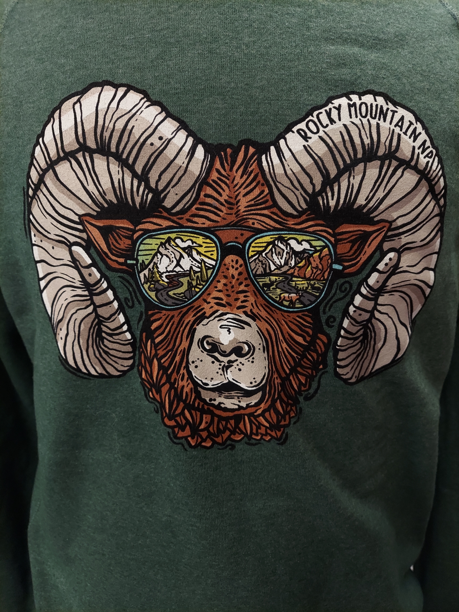 Illustration of a ram adorned in sunglasses that capture a mountain scene, paired with the text "Rocky Mountain Jam" above, featured on the Sweatshirt - RMNP Ram Sunglasses Crewneck.