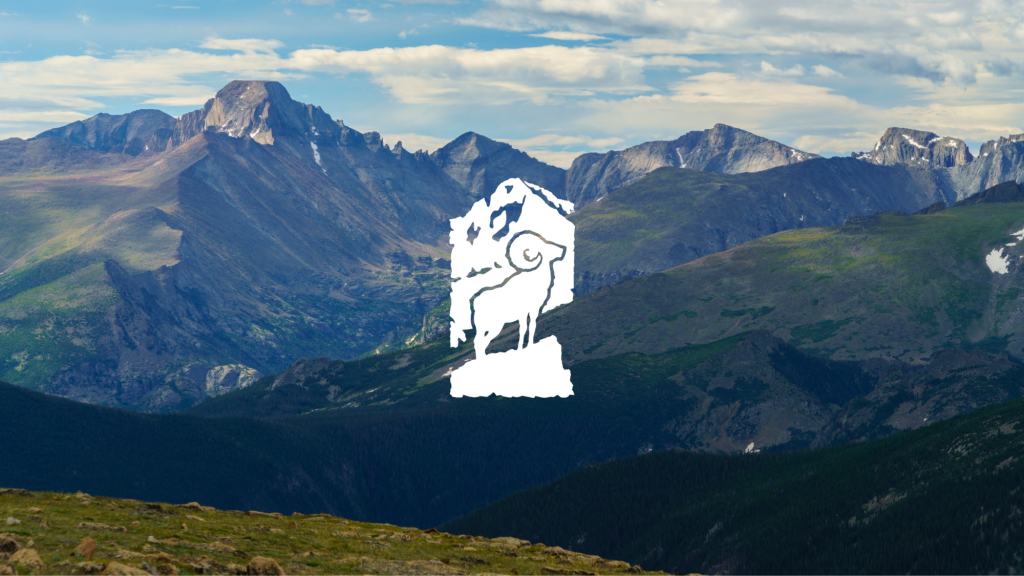 Silhouette of a bighorn sheep on a rock against a backdrop of rugged mountain peaks and a partly cloudy sky.