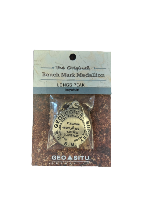 A packaged Longs Peak Summit Marker keychain includes a medallion with elevation and geographic survey details. The packaging states, "The Original Bench Mark Medallion Longs Peak Keychain.