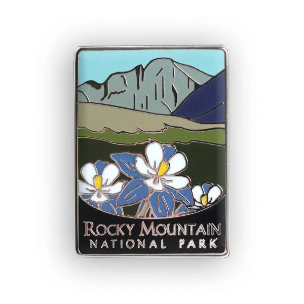 The RMNP Traveler Series pin features Rocky Mountain National Park, adorned with blue and white flowers in the foreground and stylized mountains in the background.